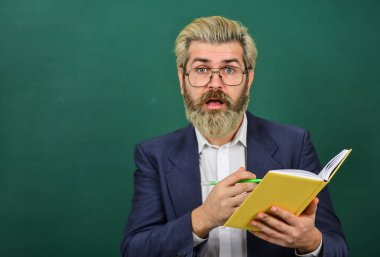 Ders kitabı olan bir öğretmen. Tecrübeli öğretmen. Uygun kurslar seçiliyor. Kitabı olan öğretmen konuyu açıklar. Kara tahtanın önündeki adam. Üniversite ve lise. Edebiyat konusu. Kitap okumak