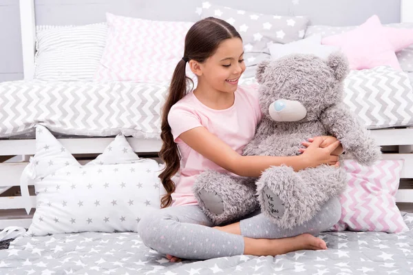 Juguete favorito. Niña abrazo osito de peluche en su dormitorio. Tiempo agradable en el acogedor dormitorio. Chica niño pelo largo lindo pijama relajarse y jugar peluche peluche oso juguete. Interacción imaginaria. Jugar juegos — Foto de Stock