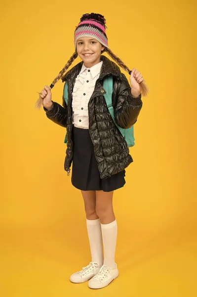 Fashion concept. Warm clothing. Buy clothes for school season. Schoolgirl fashion outfit. Fall autumn winter. Child with backpack. Fashion shop. Girl wear knitted hat and jacket yellow background — Stok fotoğraf