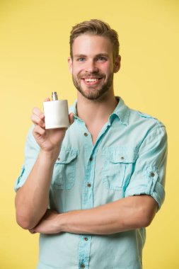 Dayanılmaz erkek kokusu. Mutlu adam parfüm şişesini sarı arka planda tutuyor. Parfüm reklamı. Eau de Tuvalet. Kozmetik ürünü. Kozmetik. Parfüm ve parfüm. Dükkan parfümü, fotokopi alanı