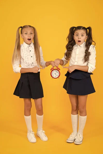 Primary school application deadline. Small children suffering from deadline stress on yellow background. Stressed little girl holding clock reminder of deadline. Deadline for submission