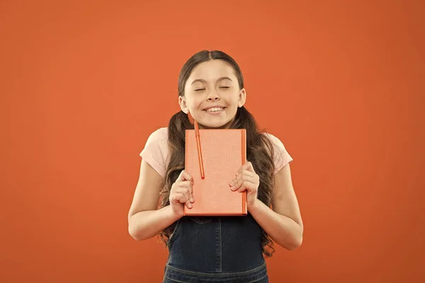 Verloren in het sprookje. literatuur les. terug naar school. notities schrijven. Kid Diary. schoolmeisje lezen boek op oranje achtergrond. poëzie en roman. modern onderwijs. Gelukkig klein meisje met notebook — Stockfoto