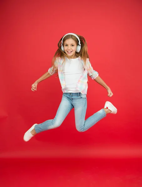 Tyle zabawy. Dziewczyna słucha muzyki nowoczesny gadżet. Dzieciak zadowolony ze skoków z bezprzewodowymi słuchawkami. Słuchawki stereo. Dzieciak korzystający z nowoczesnej technologii. Nowoczesne dziecko. Doskonały dźwięk. Niekończąca się radość — Zdjęcie stockowe