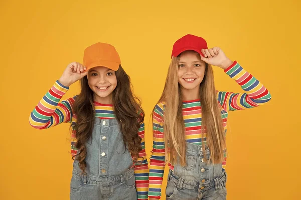 La subcultura hipster. Pequeños hipsters felices con gorras de béisbol sobre fondo amarillo. Lindos hipsters pequeños sonriendo con aspecto de moda. Adorables niños en estilo hipster —  Fotos de Stock