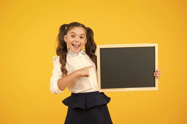 Kijk naar informatie. Kleine kind wijzende vinger op blanco Blackboard voor informatie over gele achtergrond. Klein meisje met nette schoolbord voor school informatie. Informatie voor u, kopieer ruimte — Stockfoto