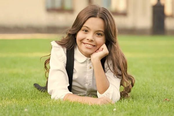 Felices vacaciones escolares. Niña feliz relajarse en la hierba verde. Niño pequeño disfrutar de la infancia feliz. Tiempo de vacaciones. Cuidado de niños después de la escuela —  Fotos de Stock