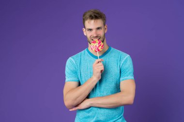 Bekarlar Günü. Tatlı yerken mutlu ol. Mutluluğun sembolü. Adam lolipop yiyor. Gülümseyen adam lolipop tutuyor. Tatil konsepti. Bekarlar için gayri resmi tatil. Guy Lolipop menekşe şekeri arka planı. Tatlı çocuk.