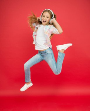 Kulaklıklı küçük kız. Hayaline ulaş. Havaya zıpla. Başarı. Kendinden geçmiş küçük kız kulaklık takıyor. Gösteri dansı hareketi. çocukluk mutluluğu. Mutlu çocuk müzik dinler. Etkinlik için enerjik şarkı