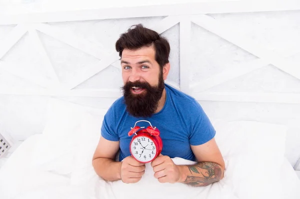 Début d'une journée géniale. Réveillez-vous tôt chaque matin. Avantages pour la santé de se lever tôt. Se lever tôt donne plus de temps. Hipster barbu homme au lit avec réveil. Il est temps de se réveiller. Habitudes saines — Photo