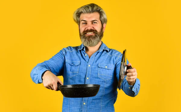 Vases de cuisson en fonte émaillée. Shopping d'ustensiles de cuisine. Des ustensiles de cuisine. Poêle antiadhésive surface en porcelaine. L'homme tient une nouvelle casserole. Cuisiner des aliments sains. Hipster barbu préparant le petit déjeuner. Conseils de friture — Photo