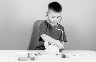 Tıp konsepti. Oyuncak ayı için tıbbi prosedürler. Tıp eğitimi. Yakışıklı çocuk, geleceğin doktor kariyeri. Sağlık hizmetleri. Küçük doktor, tıbbi aletlerle masaya oturmakla meşgul. Tıbbi muayene