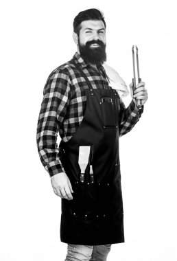 Adam mutfak aletlerini barbeküde tutuyor. Açık havada et kızartmak için aletler. Piknik ve barbekü. Parkta et pişiriyorum. Barbekü ustası. Sakallı hippi barbekü için önlük giyer. Kızartma ve ızgara yemek.