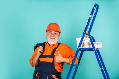 Tamir et. Kıdemli boyacı merdivende paten kullanır. Duvarı maviye boyamak. İş kıyafetleri içinde profesyonel bir ressam. Odada duvar boyama işçisi. Tekerlekli erkek dekoratör