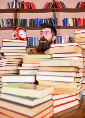 Adamım, bilim adamı çalar saatle kitap yığınlarından dışarı bakıyor. Kütüphanede çalışan sakallı bir öğretmen ya da öğrenci. Şaşırmış suratlı bir adam saate bakıyor, arka planda kitaplıklar var. Son teslim tarihi kavramı.