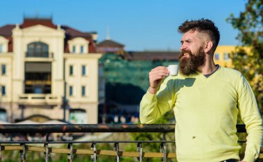 Sabah ayini konsepti. Sakallı, küçük kupalı, kahve içen bir adam. Sakallı ve bıyıklı bir adam gülen suratlı balkonda kahve içiyor, şehir arka planında, dikkati dağılmış. Uzun sakallı adam kahvenin tadını çıkar.