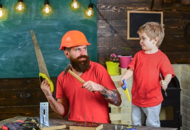 Baba, koruyucu başlıklı sakallı bir ebeveyn küçük oğluna okulda farklı aletler kullanmayı öğretiyor. Babalık kavramı. Çocuk, neşeli oyun ve babayla alet kullanmayı öğrenme..