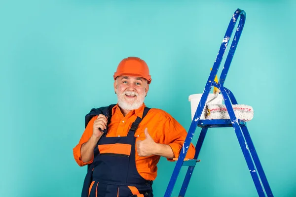 Reparieren. Seniormaler benutzt Rolle auf Leiter. Malerei der Wand in blau. professioneller Maler in Arbeitskleidung. Arbeiter streichen Wand in Raum. männliche Dekorateur Malerei mit Walze — Stockfoto