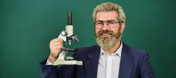 Facilitare il progresso accademico. Insegnante che cerca microscopio. Ricerca scientifica. Ricerca affascinante. Insegnante con microscopio. Uomo hipster classe lavagna sfondo. Ricerca biologica — Foto Stock