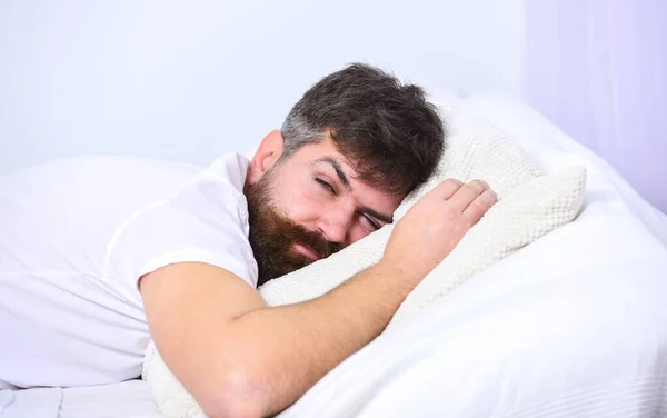 Homem de camisa deitado na cama, parede branca no fundo. Macho com barba e bigode dormindo, relaxando, dormindo, descansando. Cara cansada dormindo em lençóis brancos e travesseiro. Conceito de sesta e sesta . — Fotografia de Stock