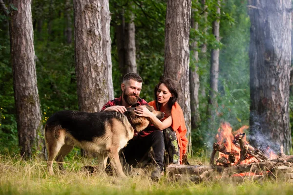 Romantikus pár kutyával ül közel tábortűz, erdő háttér. — Stock Fotó