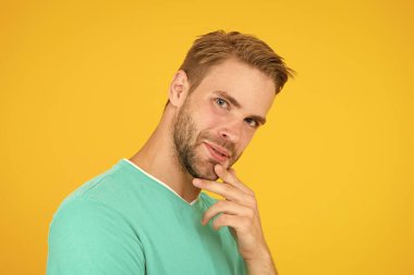 Son derece iyi görünüyor. Gözler gimlet gibi. Yakışıklı adam kendine güveniyor. Erkek yüz bakımı. Mükemmel görünüyor. Seksi sakallı adam sarı arka plan. Tıraşsız adam çeneye dokunur. Süslü tüyleri var.