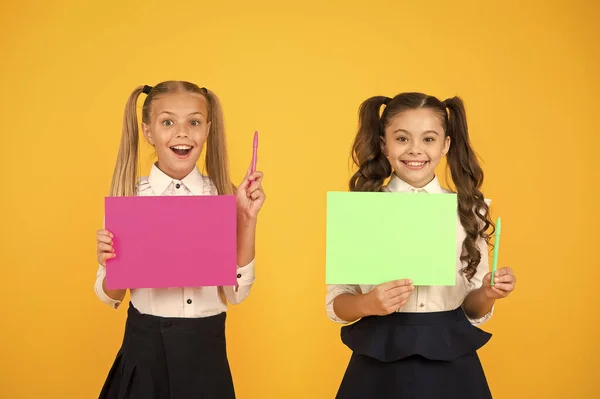 Tengo una idea. Pequeños niños lindos sonriendo de idea genio. Chicas felices sosteniendo hojas de papel para escribir idea sobre fondo amarillo. Niños pequeños con papel vacío para ideas creativas, espacio para copiar — Foto de Stock