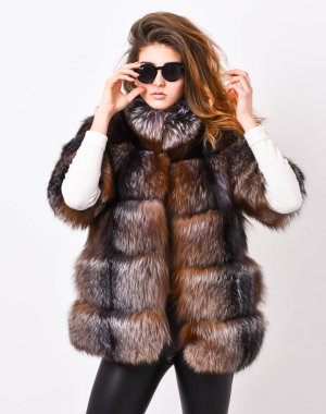 Kürk moda konsepti. Kış elit lüks kıyafetler. Dişi kahverengi kürk manto. Kürkçü modeli yakalı yumuşak tüylü paltoyla ısınıyor. Güneş gözlüğü takan ve kürk kürk giyen bir kadın.