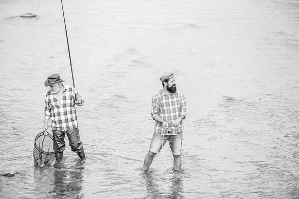 Fischerteam. Männerfreundschaft. Vater und Sohn angeln. Sommerwochenende. Glücklicher Fischer mit Angel und Netz. Hobby und sportliche Aktivität. Gemeinsam angeln. Männer stehen im Wasser. Nettes Fangkonzept — Stockfoto