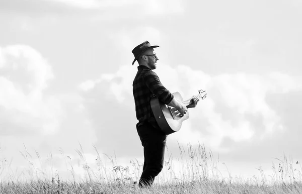 Toca una hermosa melodía. Hombre guapo con guitarra. Estilo country. Vacaciones de verano. Concepto de música country. Guitarrista cantante country de pie en el fondo del cielo de campo. Músico country inspirado. Canción de senderismo —  Fotos de Stock