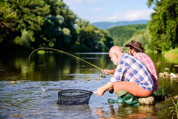 Condividere i suoi segreti. Trasferire conoscenza. Gli amici trascorrono del tempo lungo il fiume. Esperto pescatore mostra consigli al figlio. Bella serata lungo il fiume. Uomini a riva del fiume che catturano pesci. Insegnamento della pesca — Foto Stock