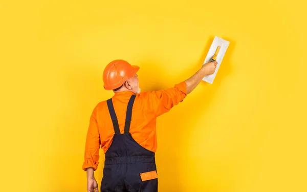 Yesero en pared de yeso uniforme de trabajo interior. Un hombre con espátula. proceso de aplicación de la capa de masilla. Herramientas de enlucido para yeso. paleta de yeso espátula sobre paneles de yeso amarillo —  Fotos de Stock