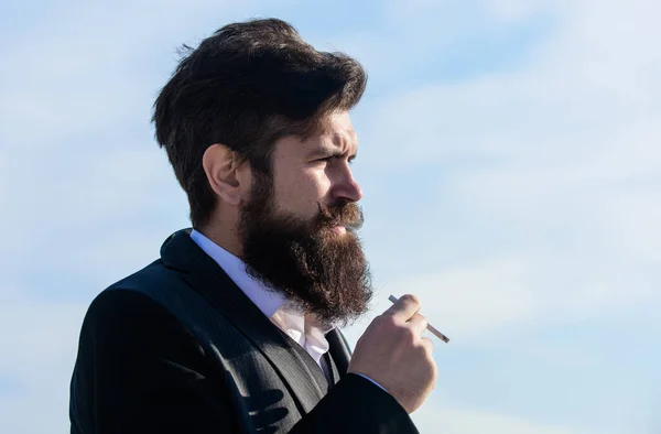 Человек с бородой и усами держит сигарету. Бородатый хипстер, курящий сигаретно-голубое небо. Парень с сигаретой наслаждается никотиновым влиянием. Правда о курении удовольствия и никотиновой зависимости — стоковое фото