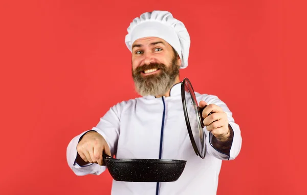Koken met passie. Een man met een baard houdt een kookpan vast. bereiden van voedsel in de keuken. Man met koksmutsen op keuken. Koken voedsel concept. Braadpan vasthouden. beste kwaliteit. baardkok in uniform met gereedschap — Stockfoto