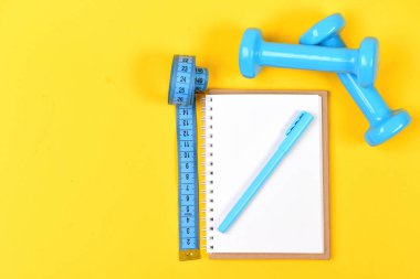 Sarı arkaplanda defter, kalem ve spor aletleri üst görünümü