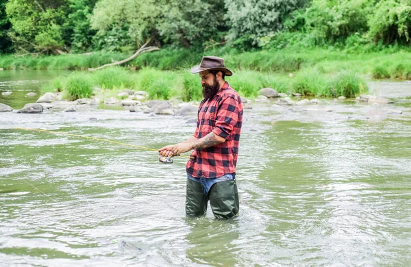 Uomo brutale indossare stivali di gomma stare in acqua del fiume. Pescatore soddisfatto. La pesca richiede di essere consapevoli e pienamente presenti nel momento. Fisher hobby maschile. Attrezzatura da pesca Fisher. Pesce sul gancio — Foto Stock