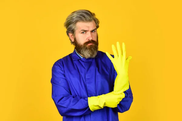 Skäggig man bär gummihandskar. mogen vaktmästare i enhetlig gul bakgrund. Vårstädning. skydda händerna med gula handskar. Förebyggande av koronavirus. Makens rena hus — Stockfoto