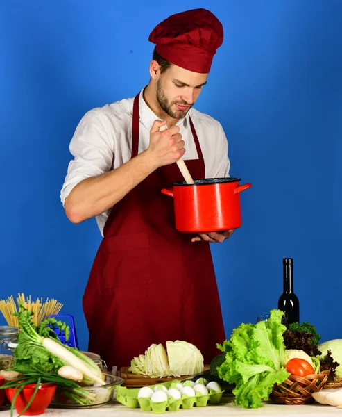 Cook stirs soup in red pot on blue background. — Stock Photo, Image