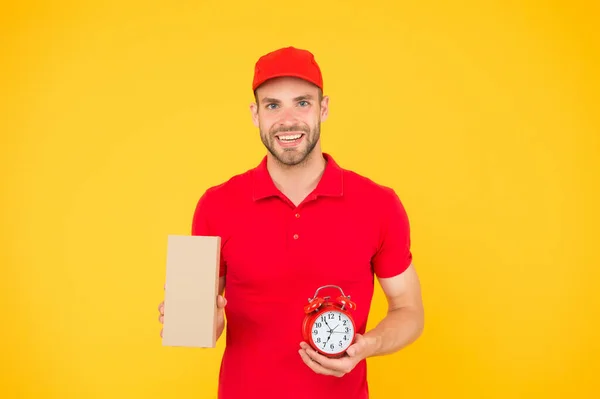 Obtenir une livraison avec nous. livraison à temps. homme en uniforme tenir boîte aux lettres et réveil. livraison pour les clients In Time. Courrier et boîte avec horloge. Livraison homme fond jaune — Photo