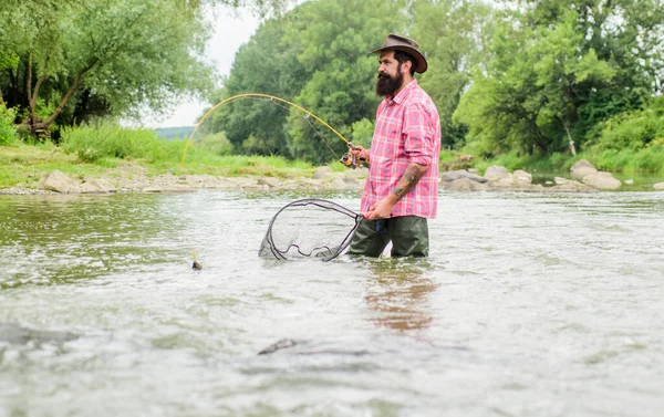 Summertime. hobby and sport activity. pothunter. mature man fly fishing. man catching fish. bearded fisher in water. fisherman with fishing rod. summer weekend. Big game fishing
