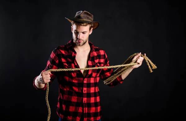 Lasso é usado em rodeios como parte de eventos competitivos. O laço pode ser amarrado ou embrulhado. A vida ocidental. Homem unshaven cowboy fundo preto. Homem de chapéu segura corda. ferramenta laço de cowboy americano — Fotografia de Stock