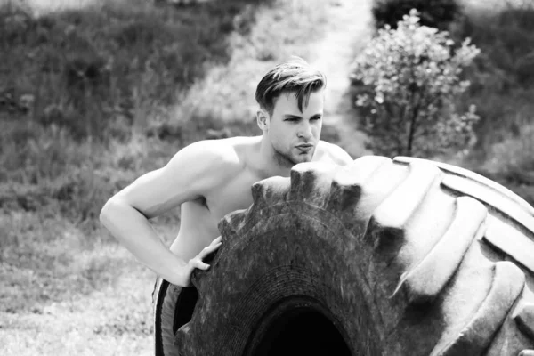 Man with serious face and naked torso pushes big tire — Stock Photo, Image