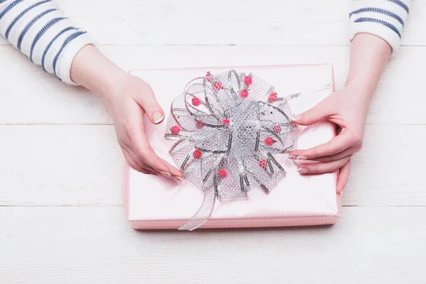 Kvinnliga händer hålla låda insvept i rosa papper med rosett — Stockfoto