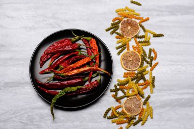 Kırmızı biber ve siyah seramik tabak içinde makarna ve malzemeler.