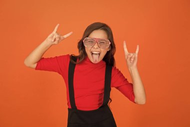 Rock partisi. Maskeli balo konsepti. Çocuk ve çizgili gözlükler. Gözlüklü, turuncu arka planda bir kız. Etkinlik ve eğlence. Parti kutlaması. Gözlük mağazası. Parti aksesuarı. Eğleniyorum.