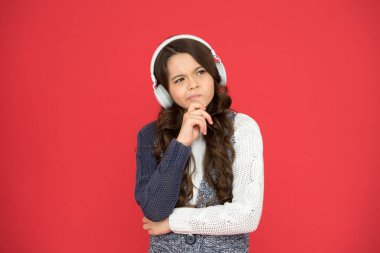 Evde eğitim. Mutlu kız kırmızı arka planda müzik dinliyor. Melodi dinlemek ve düşünmek. Ses kitabıyla çevrimiçi çalış. Küçük kız kulaklıkla şarkı dinler. Yeni teknoloji. Teknoloji ve müzik