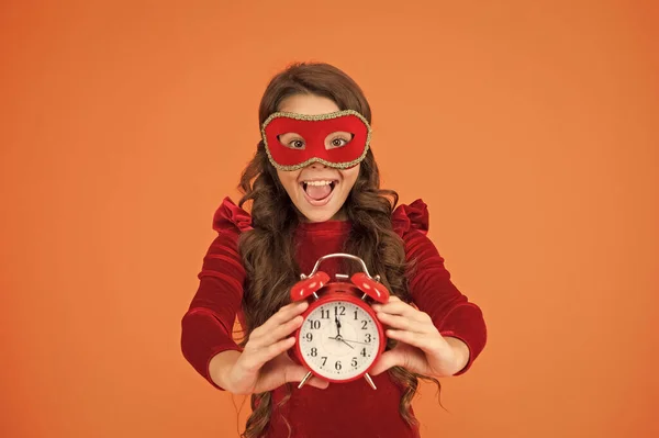 今は正しい時だパーティーの女の子は時計を見る時間。カーニバルマスクの小さな子供は目覚まし時計を保持します。12時位置だ真夜中だお祝いの時間だお祝いだクリスマスと新年 — ストック写真