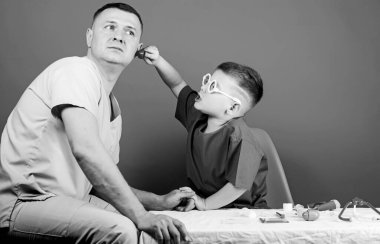 Küçük doktor, masada tıbbi aletlerle oturuyor. Hastalık tedavisi. Baba ve oğul tıp hanedanlığı. Tıbbi muayene. Tatlı çocuk ve babası doktor. Hastane çalışanı. Sağlık hizmetleri. Tıp konsepti