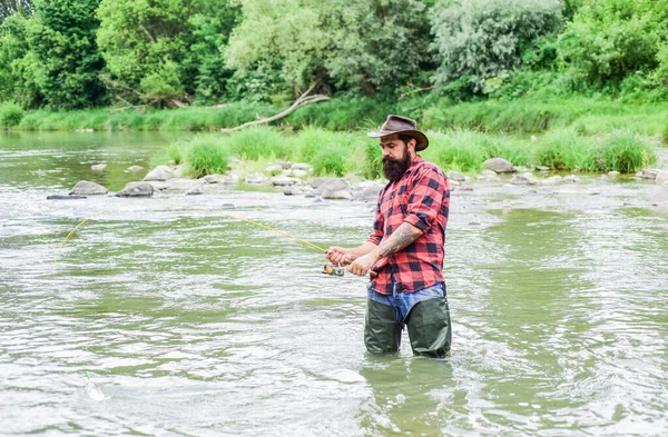 Pescador satisfecho. Pasatiempo masculino Fisher. Equipo de pesca Fisher. Pescado en gancho. La pesca requiere que usted sea consciente y totalmente presente en el momento. Hombre brutal usar botas de goma de pie en el agua del río — Foto de Stock