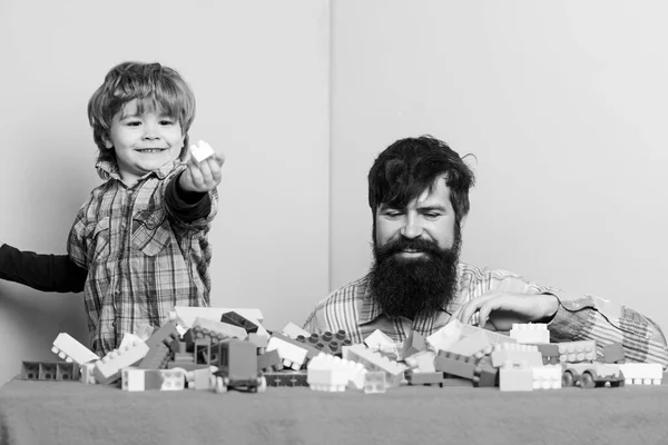 Vousatý otec a chlapec si spolu hrají. Otec syn hraje hru. Táta a děcko postavili plastové bloky. Otec a syn vytvářejí barevné konstrukce z cihel. Vývoj a výchova dětí — Stock fotografie