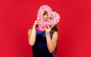 Sevimli kız eğleniyor. Romantik bir ruh hali. Mutlu çocuk kalbini kırmızı arka planda tut. Pembe kalpli küçük bir kız. Kalp şeklinde dekoru olan sevgililer günü. Sevgi ve ilgi tatili. Sevildiğimi hissetmek. Güzel bebek.